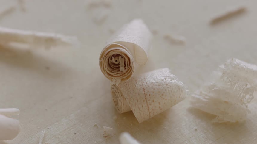 A tight curl of wood shavings falls onto another one