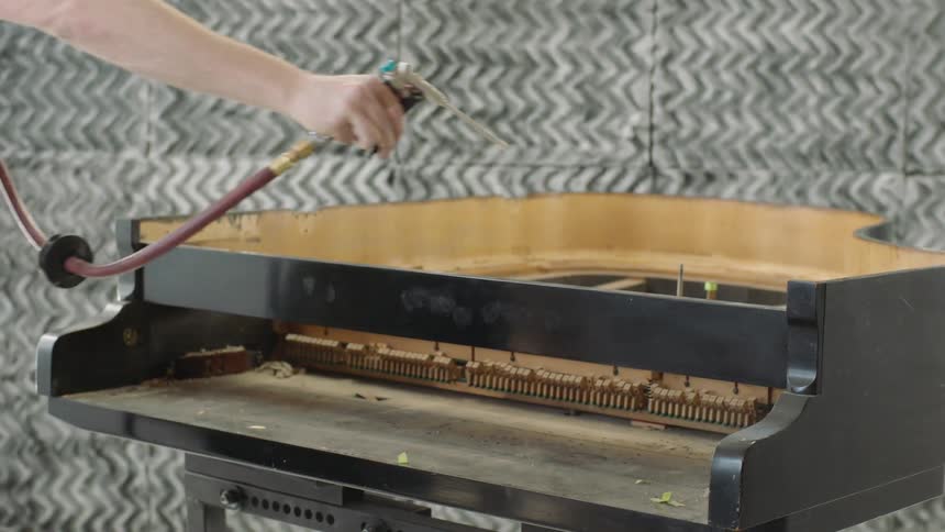 A technician uses an air compressor to clean the intricate inner workings of a grand piano