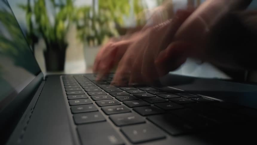 A mans hands are typing incredibly fast on a laptop keyboard