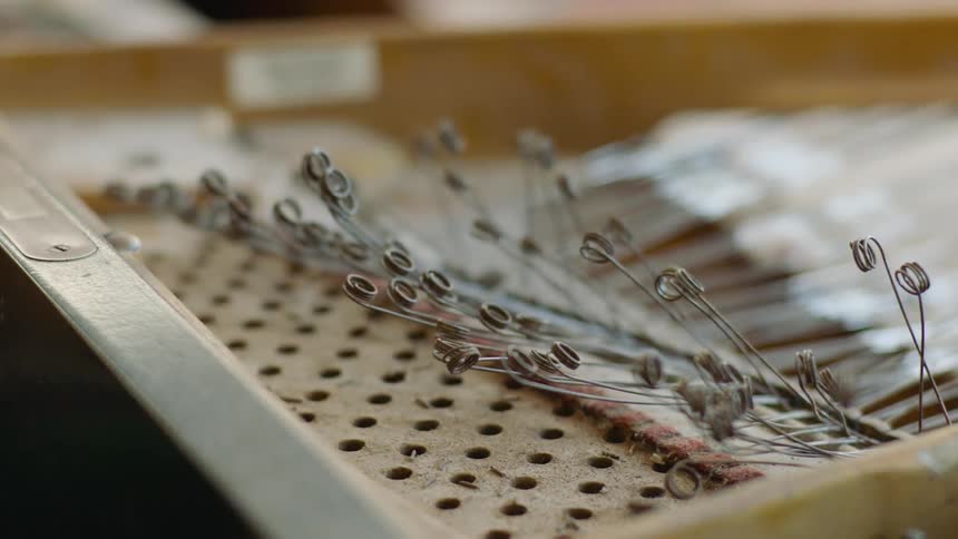 Wires with the ends coiled are on a pegboard in a wooden frame