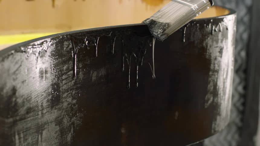 Varnish drips from a paintbrush as it moves along the edge of the wood