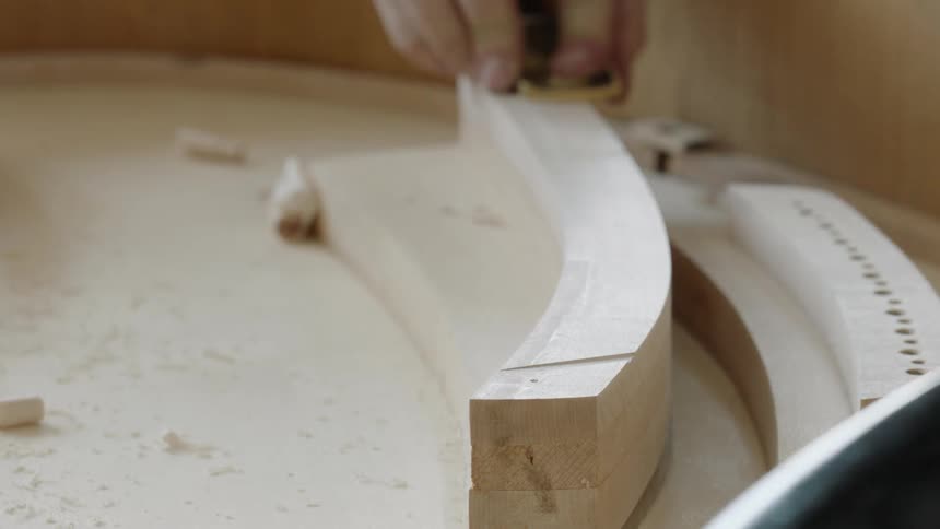 A mans hand cuts wood on an unfinished piece of wooden furniture