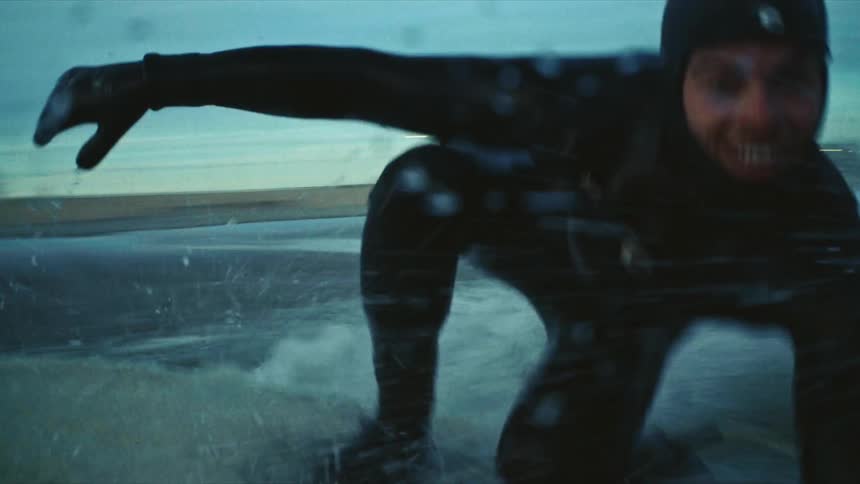 A person is surfing on a wave in the ocean during early morning or late evening with the city skyline visible in the background