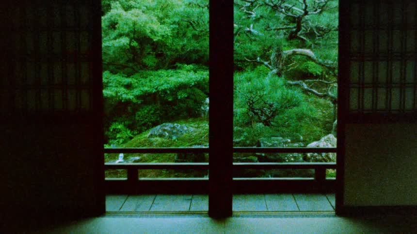 The balcony of a house is shown through its open doors which shows a forest behind it