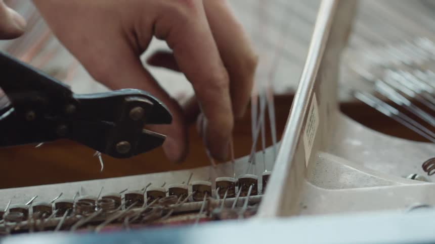 A person is cutting wires on a piano as they assemble it