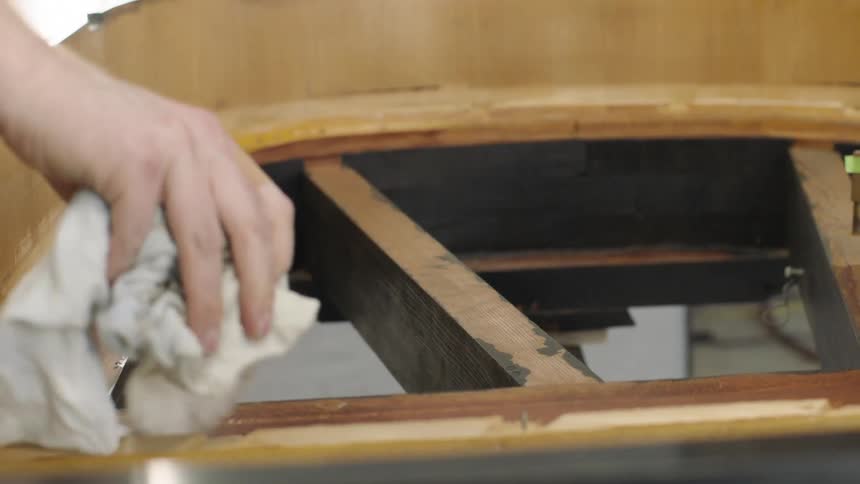 A mans hand holds a washcloth and wipes down a wooden object that is in the process of being built