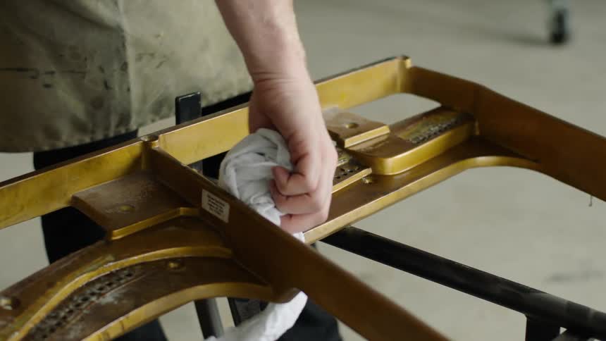 Hand cleaning a gold metal structure with a white cloth in a workshop environment
