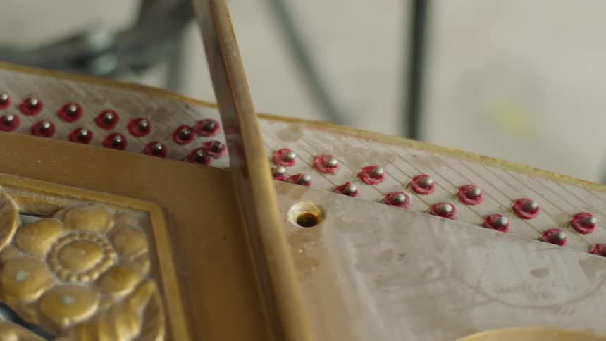A person is replacing a red felt piece on the interior of a piano