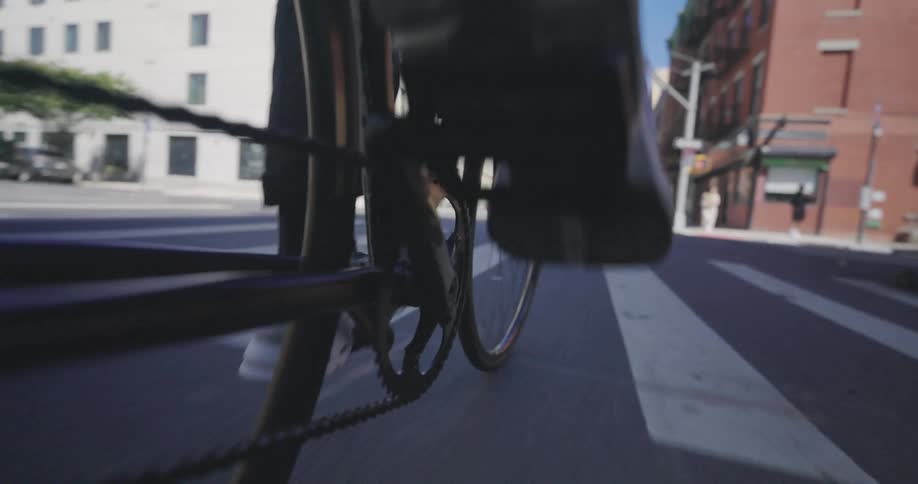 A persons feet are shown riding a bicycle down a city street