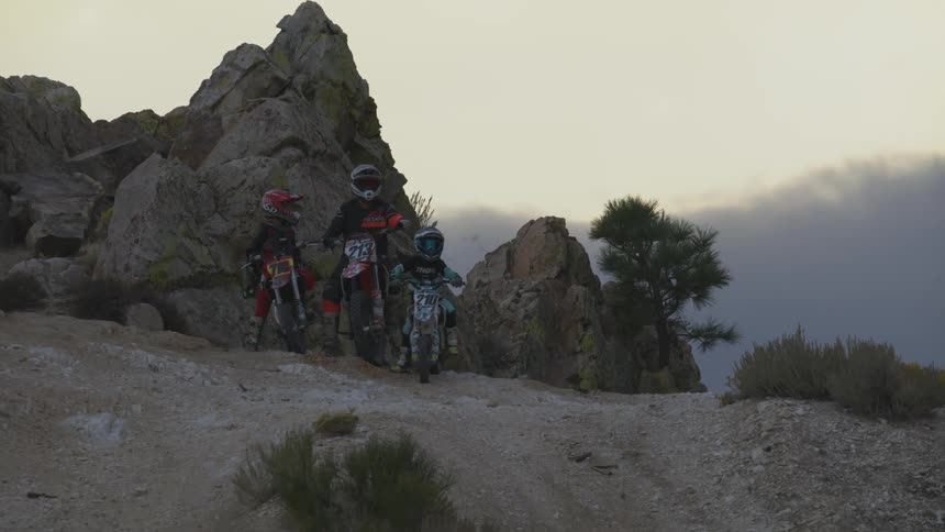 Two kids and an adult on motocross bikes on top of a hill