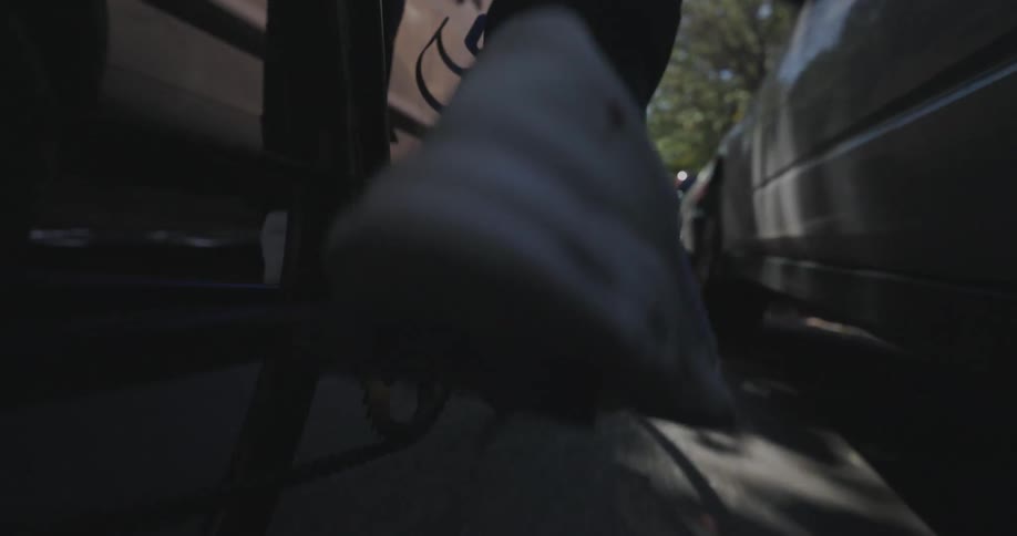 A close dynamic shot of a persons foot pedaling a bicycle with the focus on the chain and pedal as they move through a city street