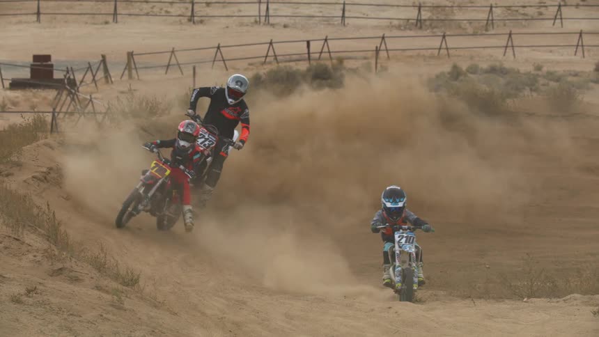 Boys are racing their dirt bikes on a sloped dirt track