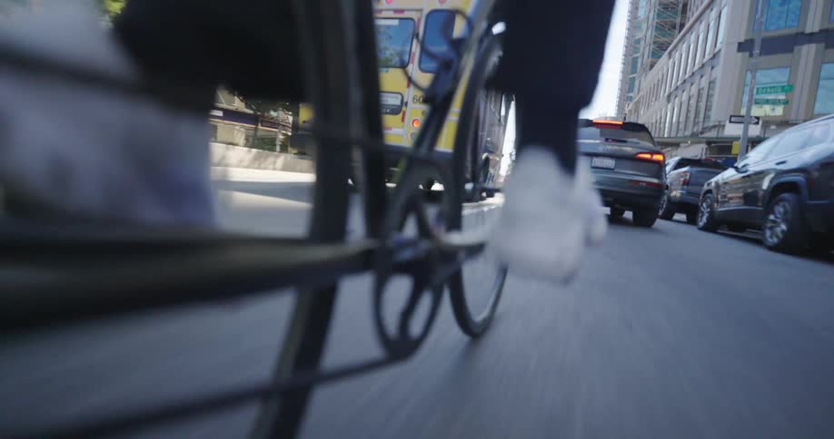 A close dynamic shot of a persons foot pedaling a bicycle with the focus on the chain and pedal as they move through a city street