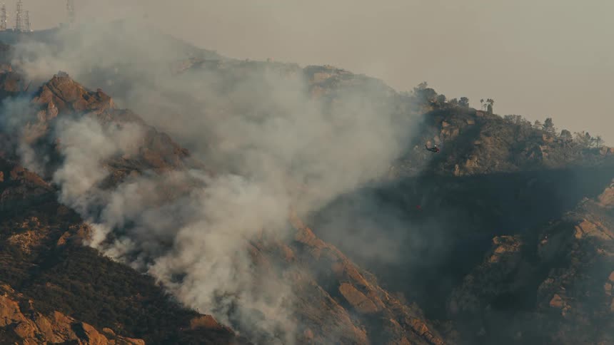 A helicopter flies through the smoke of the burning trees on the mountain