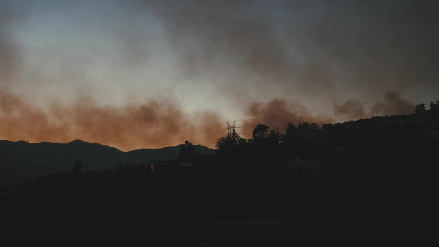 A dense plume of smoke billows over a dark mountainous landscape at dusk