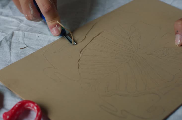 A hand is using a carving tool to engrave a design into a piece of wood or linoleum