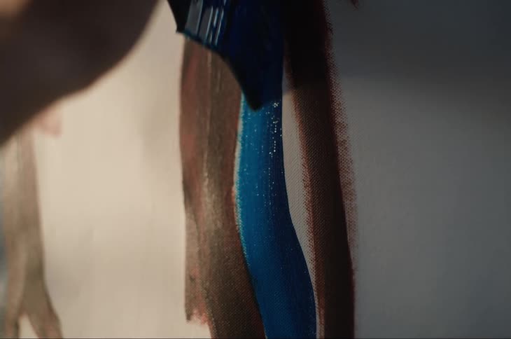 Hand holding a paintbrush and painting a picture with a blue paint