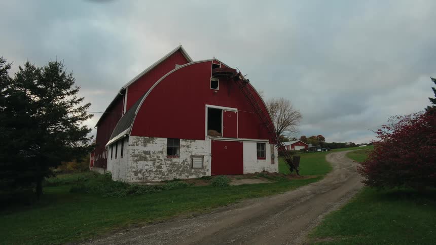 A red barn with a white lower section along a dirt road under a cloudy sky