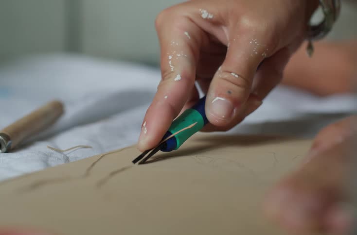 A hand is using a carving tool to engrave a design into a piece of wood or linoleum