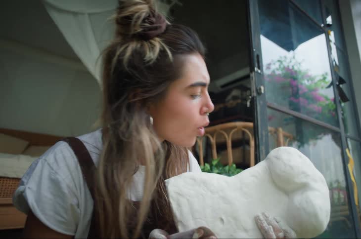 A woman sitting in a doorway is using a cloth on a statue she sculpted