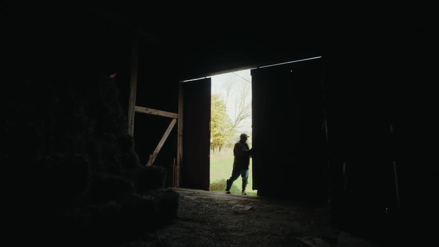 A farmer opens the door to the barn letting in sunlight