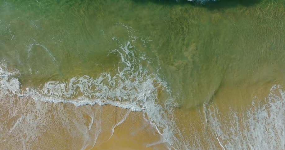 Aerial view of sea waves with foam reaching the wet sand of the beach