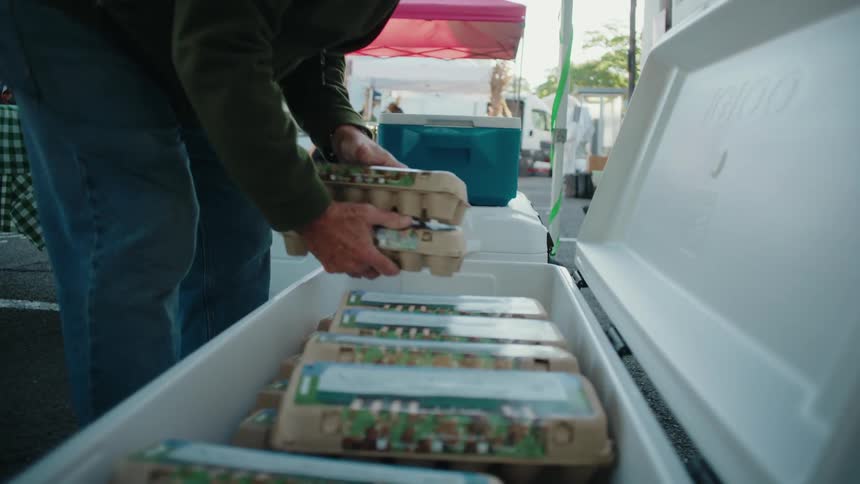 A man is taking egg cartons out of a cooler at a stand in a farmers market