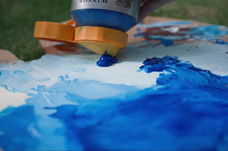 Blue paint is being squeezed from a container over a palette