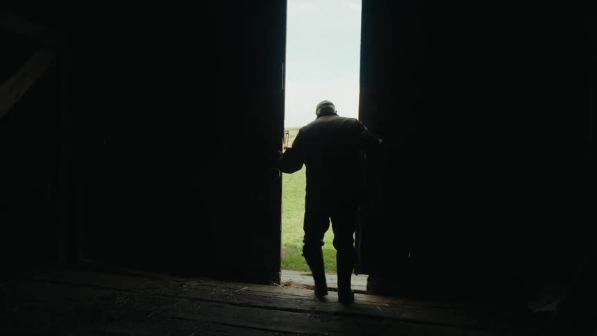 Man closing the doors of a dark shed onto an open sunny field