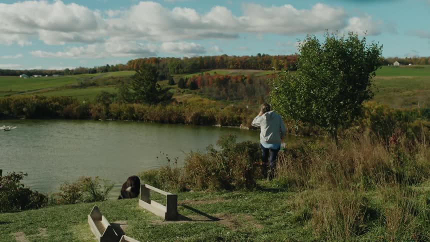 The dog follows a woman carrying a bucket to the pond