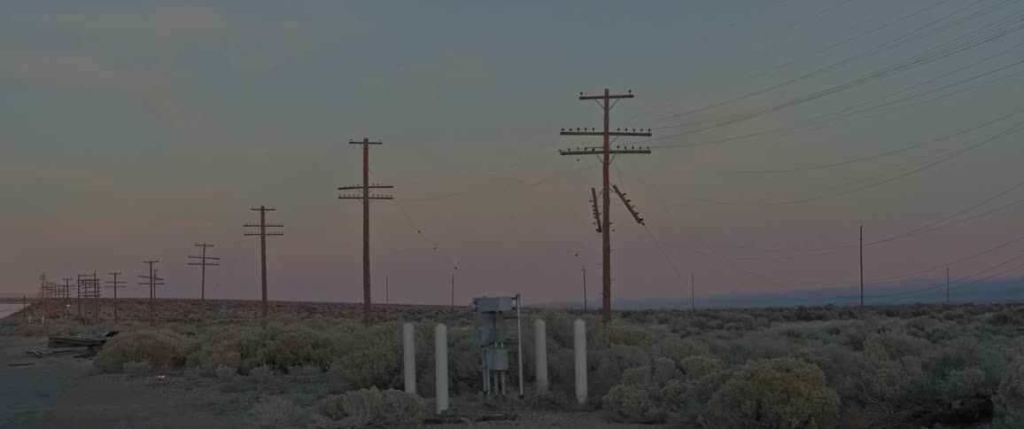 Power lines stretching along wooden poles in a desert landscape with scrub vegetation