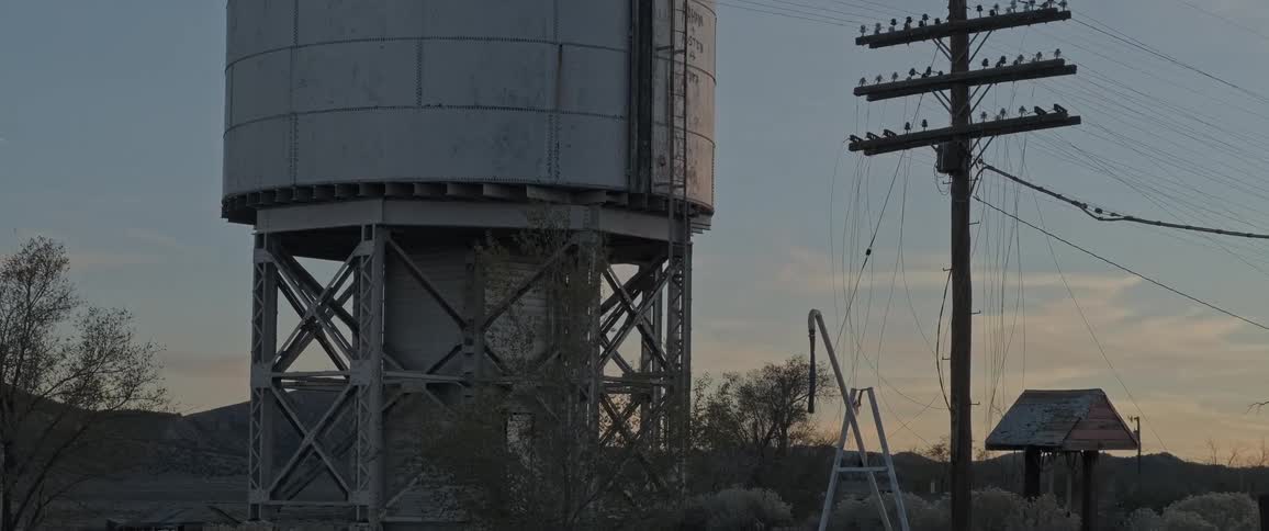 A large water tower stands tall against a twilight sky with a power pole nearby