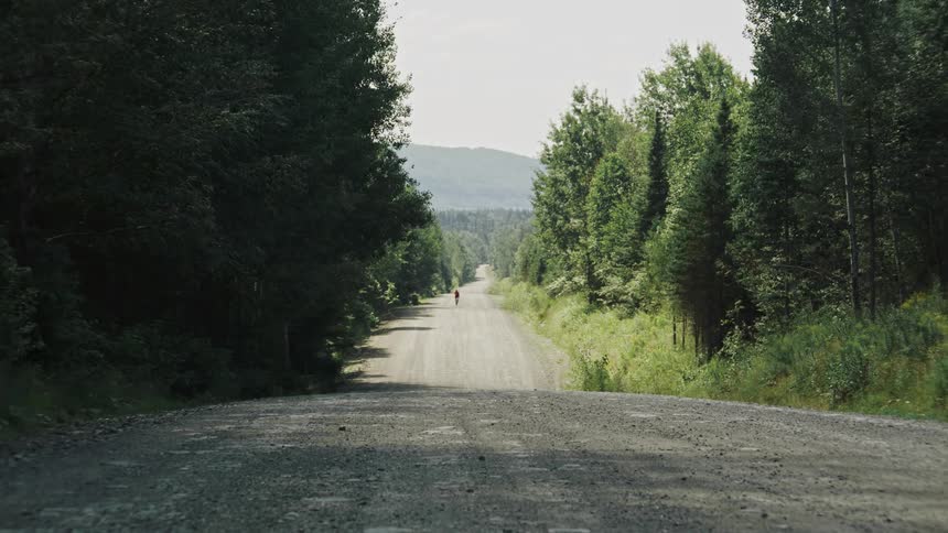A lone gravel cyclist riding far away on a long straight gravel road stretching into the distance