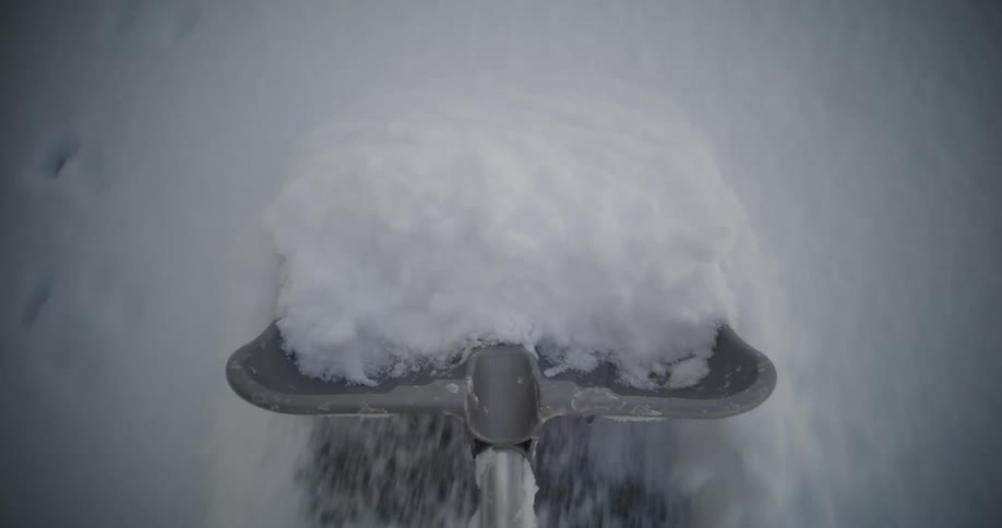 A person is using a metal shovel to remove snow from the sidewalk