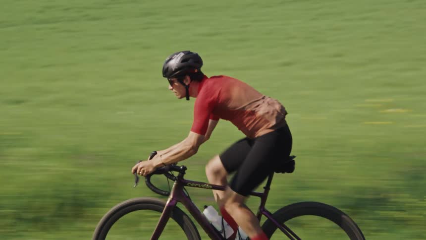 Follow of a gravel cyclist pedalling at high speed through a green field