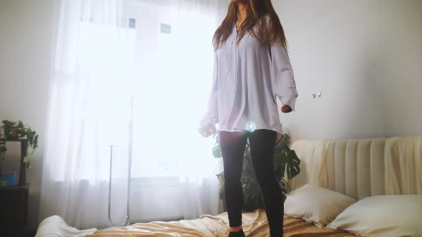 A female with long brown hair jumping on a bed