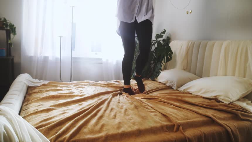 A woman spins as she jumps on a bed in a bedroom