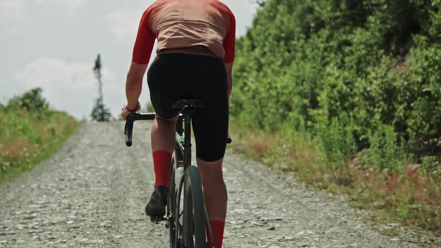 Zoom-in on the buttom of a gravel cyclist going up a dirt road in the mountain at midday