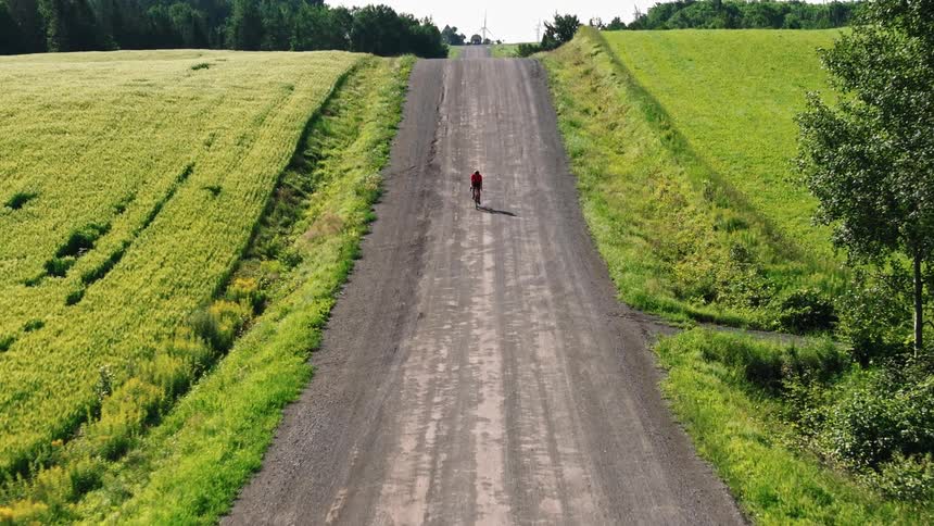 Drone shot of a man riding a gravel bike on a dirt road in the countryside
