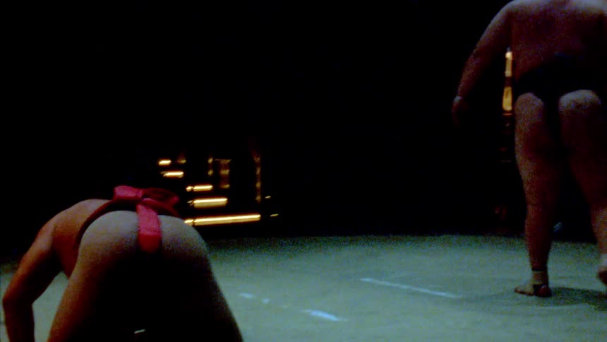 Sumo wrestlers engage in a match on a dimly lit arena