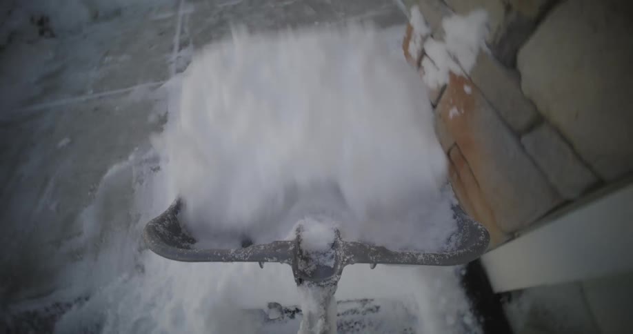 A person shovels snow from the sidewalk next to a building