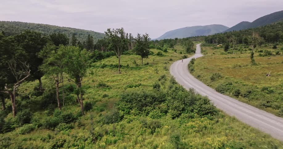 Reveal of a lone cyclist riding along a winding gravel road surrounded by lush green vegetation and rolling hills in a rural landscape