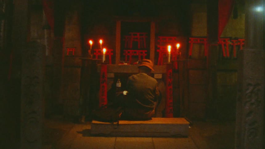 A man is sitting on a bench facing an altar in a shrine