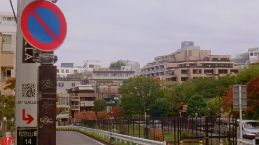 A narrow urban street lined with apartment buildings and small businesses winds its way through a densely populated neighborhood