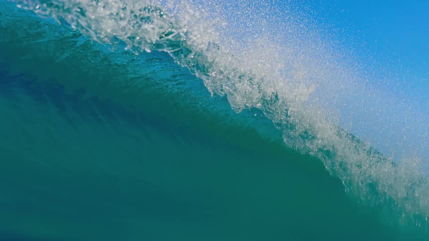 A powerful ocean wave crashes in clear blue water under a bright blue sky