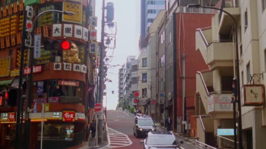 A steep street lined with colorful shops and neon signs winds through a japanese city