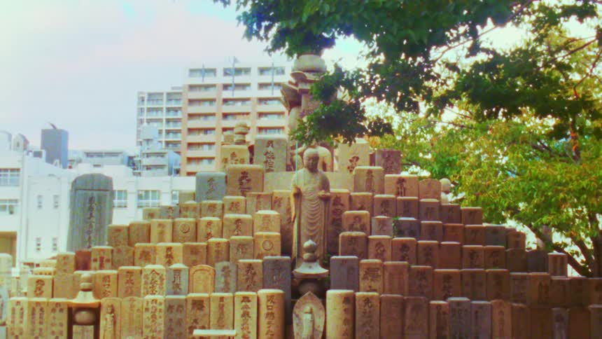 A stone monument with numerous engraved tablets and statues stands in an urban setting in japan