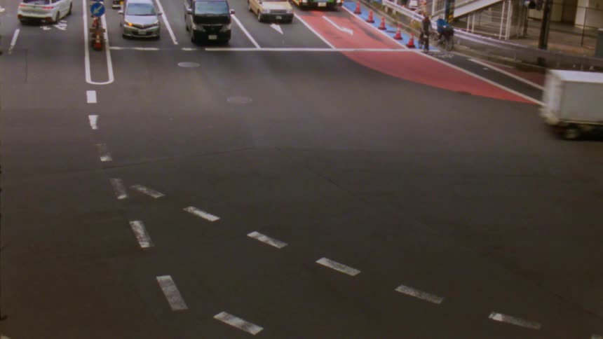 A busy urban intersection features multiple vehicles and a cyclist on the sidewalk