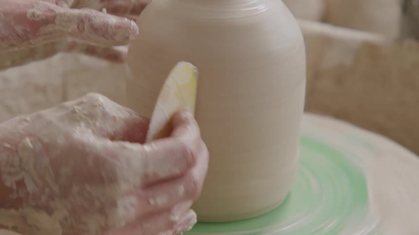 A potters hands carefully smooth and shape a clay vessel on a spinning wheel