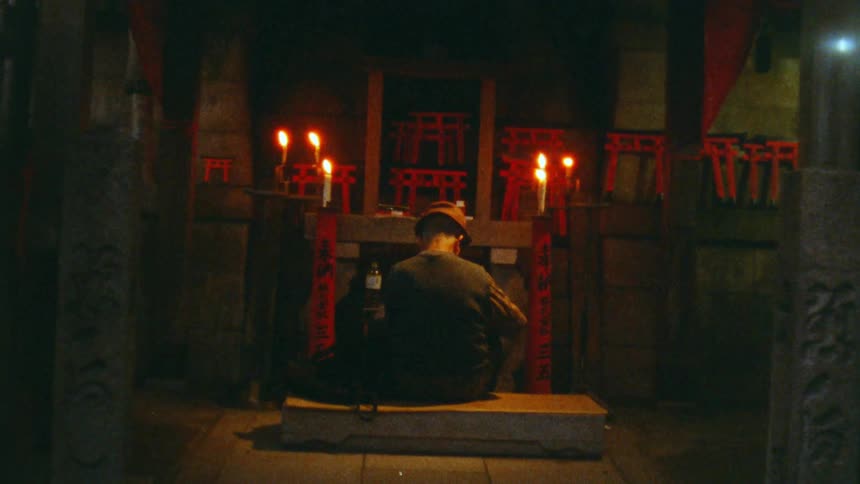 A man is sitting in front of a shrine with lit candles on it